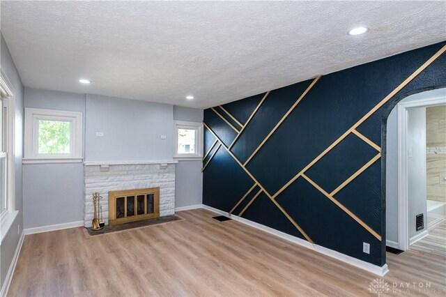 unfurnished living room with a stone fireplace, hardwood / wood-style floors, and a textured ceiling