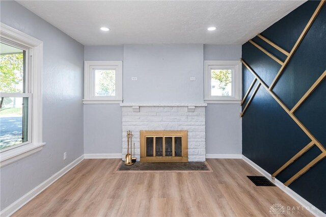 unfurnished living room featuring a stone fireplace, a healthy amount of sunlight, and wood-type flooring