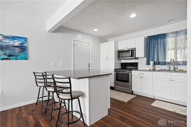 kitchen with white cabinets, a kitchen breakfast bar, dark hardwood / wood-style flooring, and stainless steel appliances