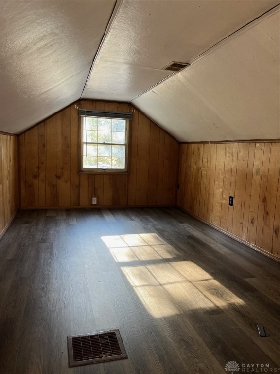 bonus room with a textured ceiling, dark hardwood / wood-style flooring, vaulted ceiling, and wood walls