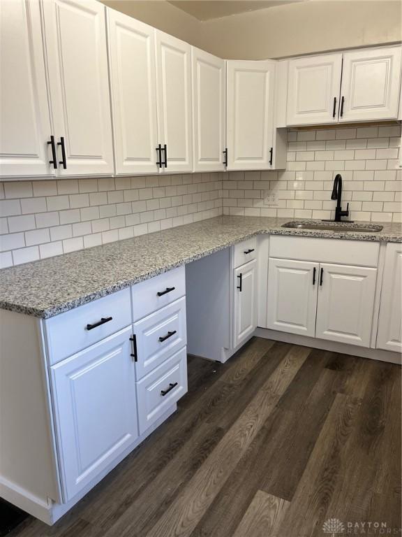 kitchen featuring sink, light stone counters, dark hardwood / wood-style flooring, decorative backsplash, and white cabinets