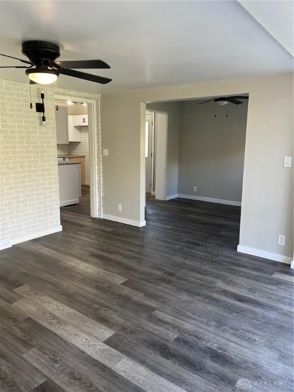 unfurnished living room featuring ceiling fan, brick wall, and dark hardwood / wood-style flooring