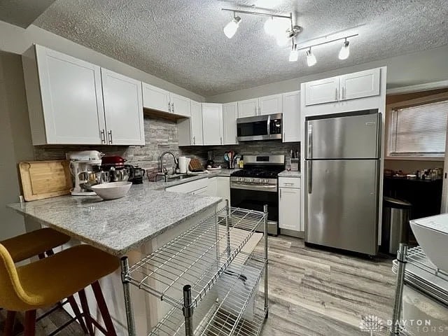 kitchen featuring tasteful backsplash, appliances with stainless steel finishes, sink, kitchen peninsula, and white cabinets