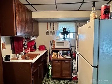 kitchen featuring sink, a drop ceiling, dark brown cabinets, and white appliances