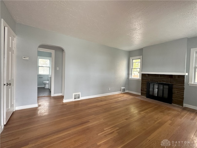 unfurnished living room with a stone fireplace, a wealth of natural light, dark wood-type flooring, and a textured ceiling