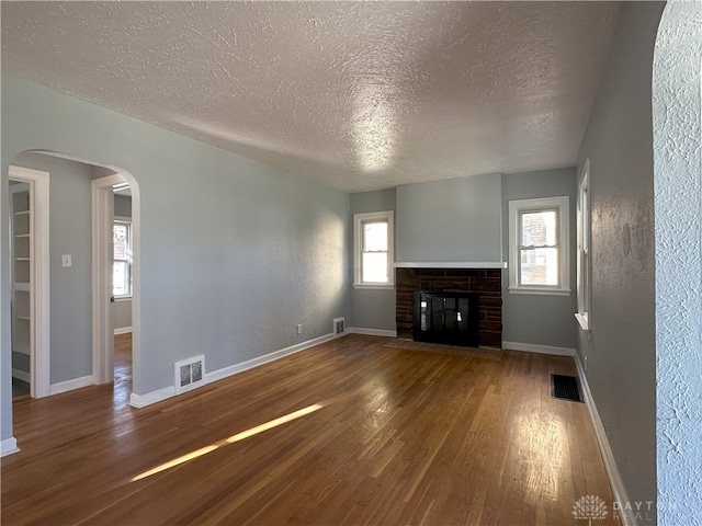 unfurnished living room with a stone fireplace, wood-type flooring, a textured ceiling, and a wealth of natural light