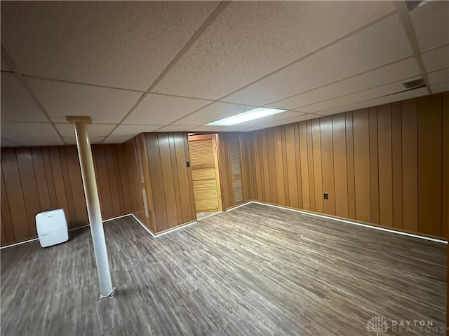 basement featuring a drop ceiling, wood walls, and dark wood-type flooring