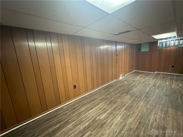 basement featuring a paneled ceiling, wood walls, and dark wood-type flooring