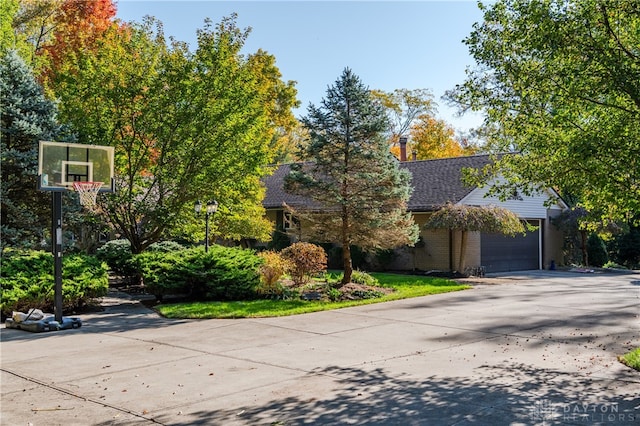 obstructed view of property featuring concrete driveway, a chimney, roof with shingles, an attached garage, and brick siding