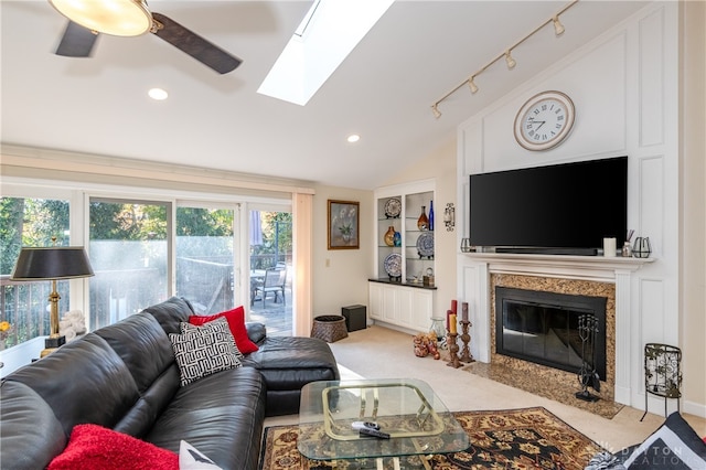 carpeted living room with rail lighting, ceiling fan, vaulted ceiling with skylight, and a high end fireplace