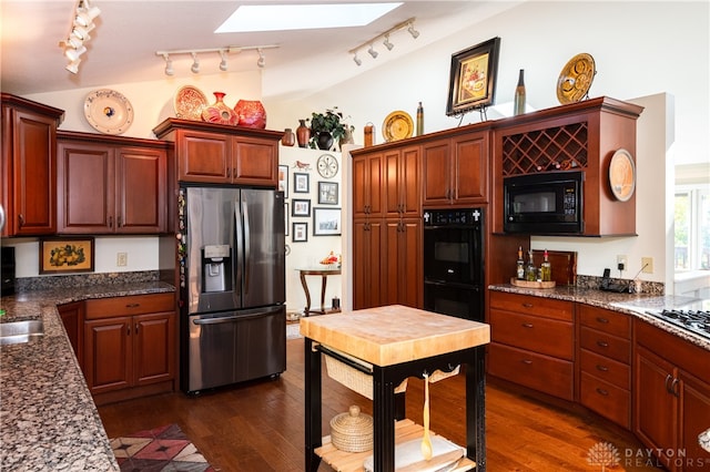 kitchen with track lighting, dark hardwood / wood-style flooring, dark stone counters, black appliances, and a skylight