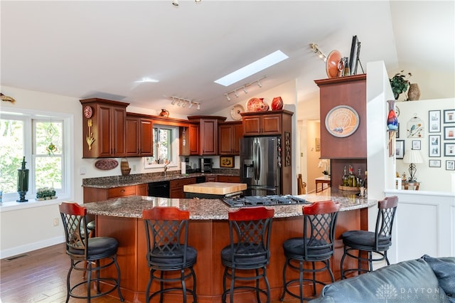 kitchen with dark hardwood / wood-style floors, kitchen peninsula, stainless steel appliances, sink, and lofted ceiling with skylight