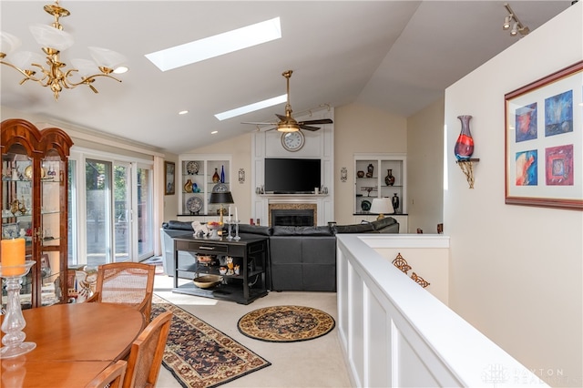 living room with vaulted ceiling with skylight and ceiling fan with notable chandelier