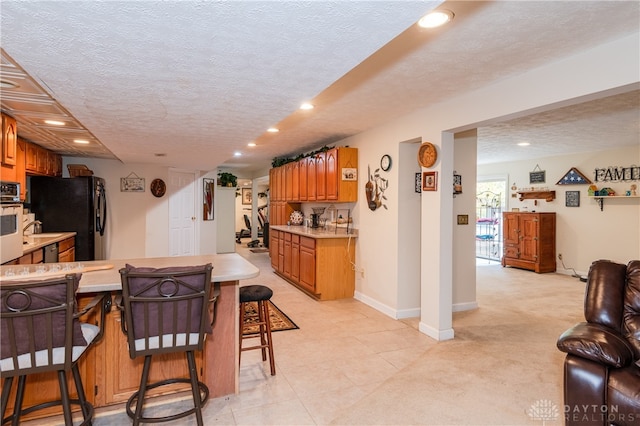 kitchen with oven, black refrigerator, kitchen peninsula, a breakfast bar, and a textured ceiling