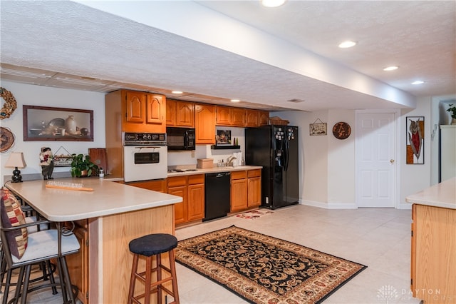 kitchen featuring kitchen peninsula, a kitchen breakfast bar, a textured ceiling, black appliances, and sink