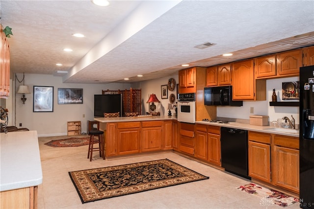 kitchen with kitchen peninsula, sink, black appliances, a breakfast bar, and a textured ceiling