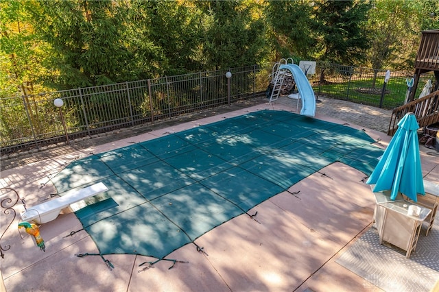 view of swimming pool with a patio area, a water slide, and a diving board