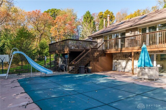 view of pool featuring a wooden deck, a water slide, and a patio area