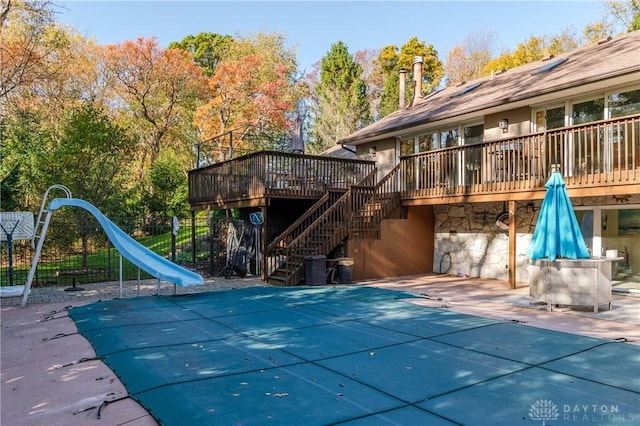 view of pool with stairway, a patio area, fence, a deck, and a water slide