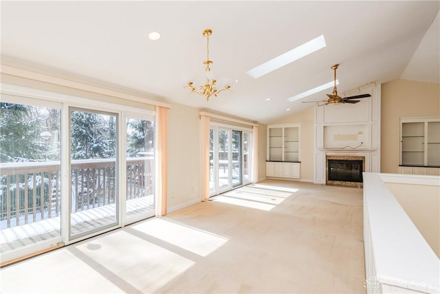 unfurnished living room featuring vaulted ceiling with skylight, baseboards, light colored carpet, a fireplace, and ceiling fan with notable chandelier