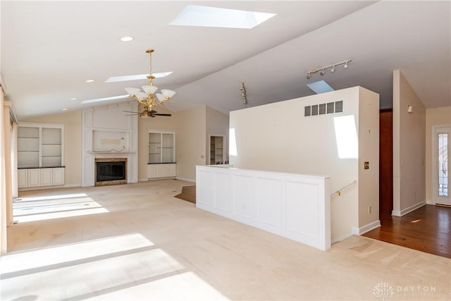 unfurnished living room with a fireplace, visible vents, a ceiling fan, track lighting, and vaulted ceiling with skylight