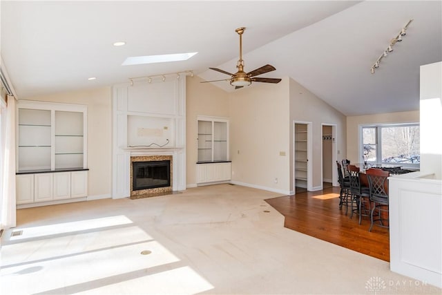 living room featuring vaulted ceiling with skylight, light carpet, a fireplace, baseboards, and track lighting