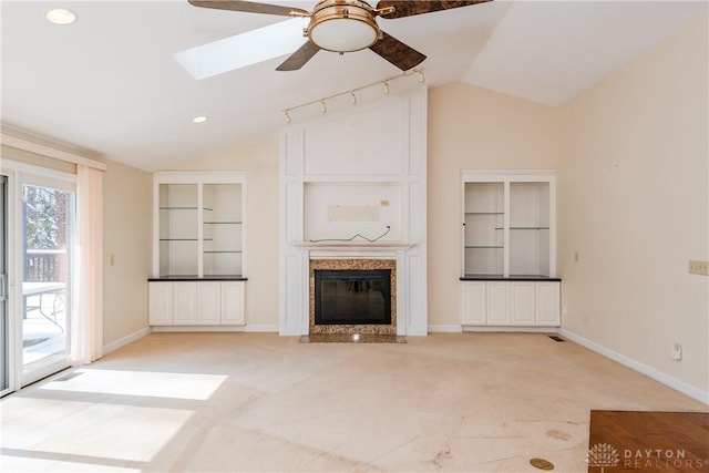 unfurnished living room with lofted ceiling with skylight, a high end fireplace, light carpet, and baseboards