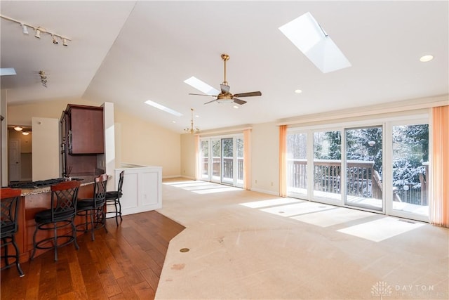 living area featuring a ceiling fan, baseboards, dark wood-style floors, lofted ceiling with skylight, and rail lighting