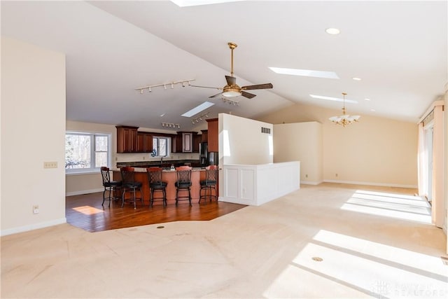 kitchen with lofted ceiling with skylight, open floor plan, a kitchen island, a kitchen bar, and ceiling fan with notable chandelier