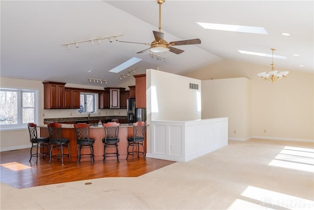 kitchen with light wood finished floors, visible vents, lofted ceiling with skylight, a kitchen bar, and ceiling fan with notable chandelier