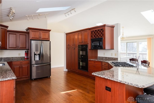 kitchen featuring vaulted ceiling with skylight, a breakfast bar, light stone countertops, dark wood-style floors, and black appliances