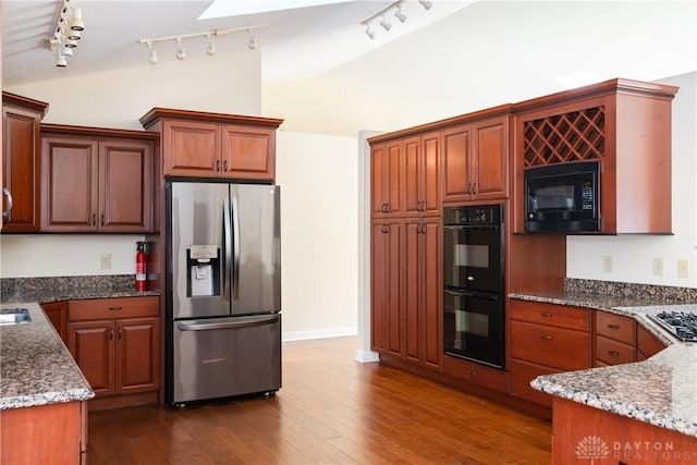 kitchen with lofted ceiling, black appliances, dark stone countertops, and dark wood-style floors