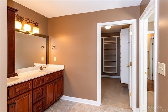 full bath featuring double vanity, a spacious closet, a sink, and baseboards