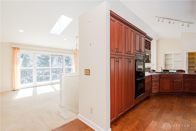 kitchen with light wood finished floors, vaulted ceiling with skylight, baseboards, stainless steel appliances, and track lighting