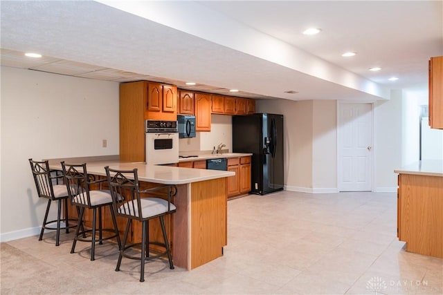 kitchen with a breakfast bar, brown cabinets, light countertops, black appliances, and baseboards