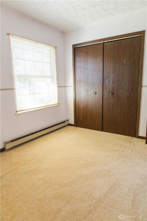 unfurnished bedroom featuring a textured ceiling, a baseboard heating unit, light colored carpet, and a closet