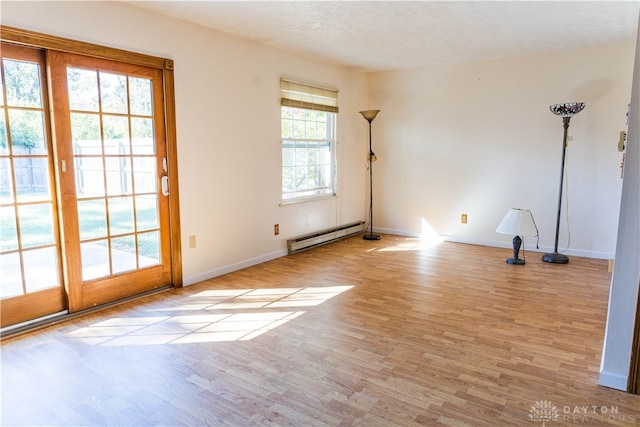 spare room featuring light hardwood / wood-style flooring, a baseboard heating unit, and plenty of natural light