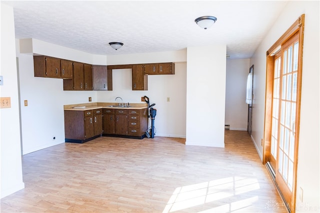 kitchen with sink, a textured ceiling, dark brown cabinets, and light wood-type flooring