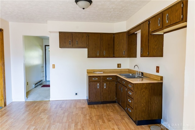 kitchen featuring a textured ceiling, baseboard heating, sink, and light wood-type flooring