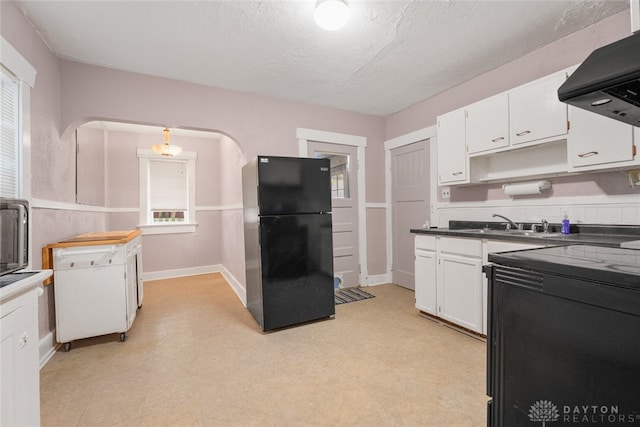 kitchen featuring black fridge, hanging light fixtures, ventilation hood, white cabinetry, and a textured ceiling