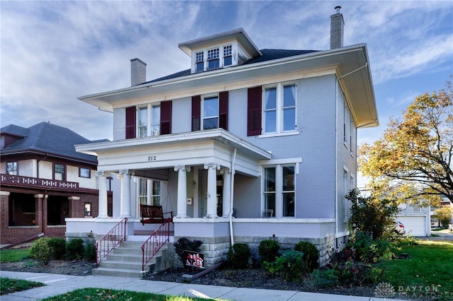 american foursquare style home with covered porch, a chimney, and brick siding