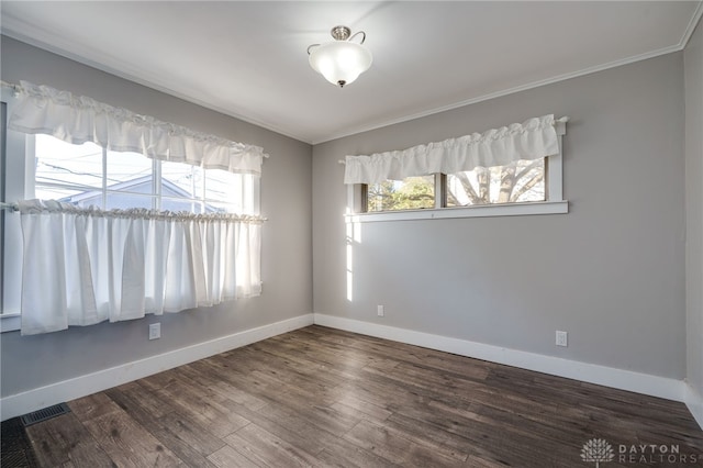 empty room featuring a wealth of natural light, visible vents, baseboards, and wood finished floors