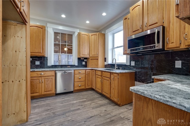 kitchen with appliances with stainless steel finishes, a sink, light wood-style flooring, and crown molding