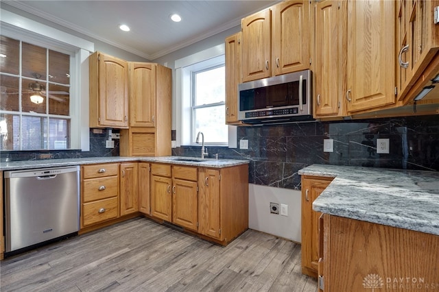 kitchen with a sink, light wood-style floors, ornamental molding, appliances with stainless steel finishes, and decorative backsplash