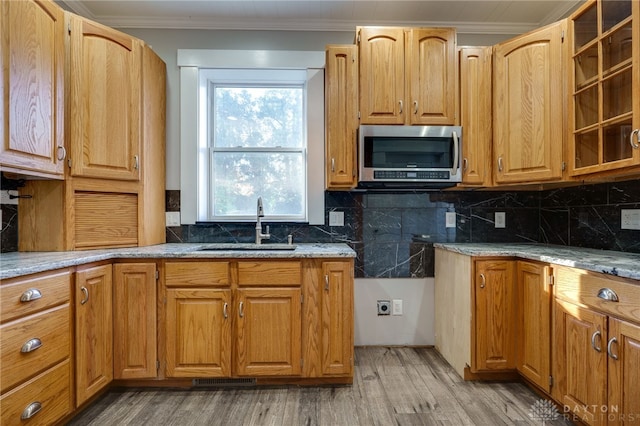 kitchen with crown molding, stainless steel microwave, decorative backsplash, and a sink