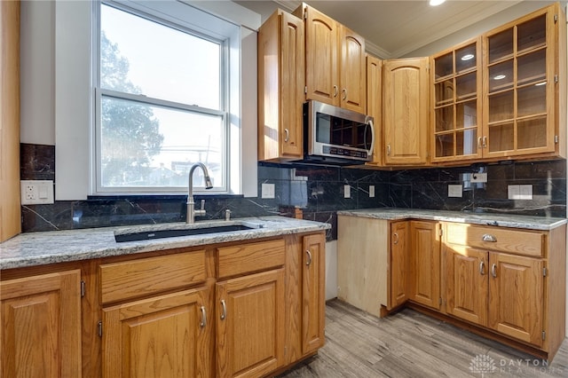 kitchen featuring glass insert cabinets, stainless steel microwave, backsplash, and a sink