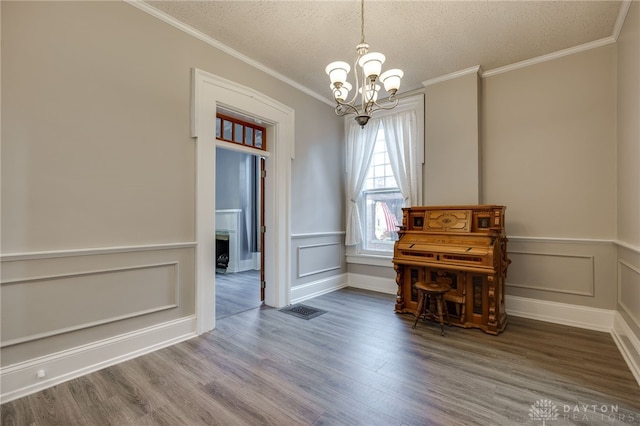 unfurnished dining area featuring a textured ceiling, ornamental molding, wood finished floors, and a notable chandelier