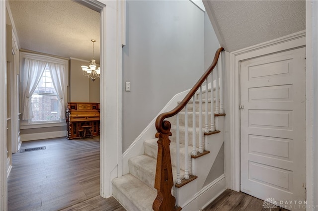 stairway featuring a textured ceiling, wood finished floors, visible vents, and an inviting chandelier