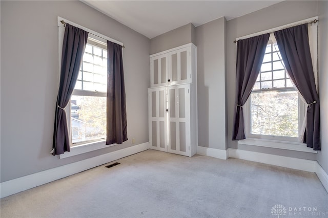 carpeted spare room with baseboards, visible vents, and a wealth of natural light