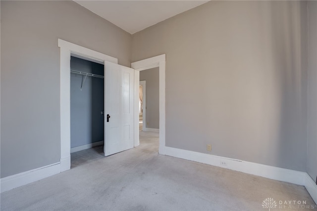 unfurnished bedroom with a closet, light colored carpet, and baseboards